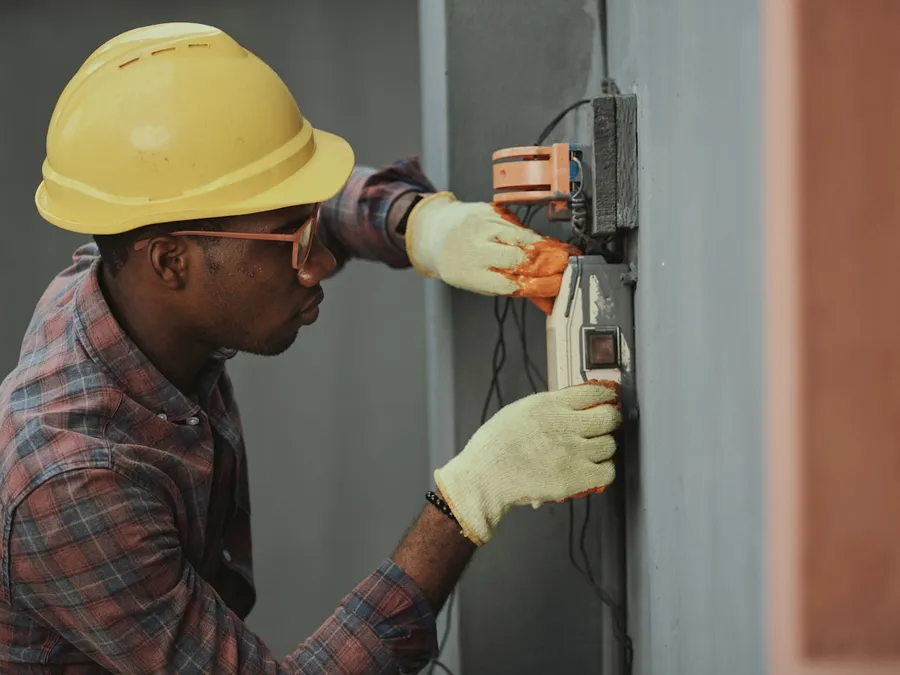 An electrician in a hard hat wires a service panel