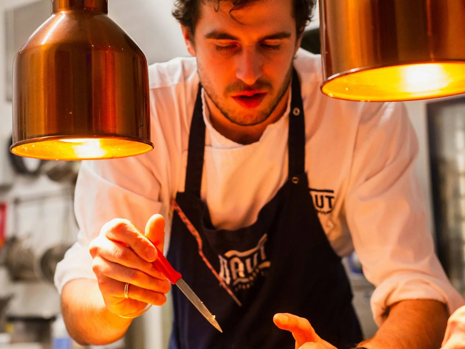A chef plates a dish under warm copper heat lamps
