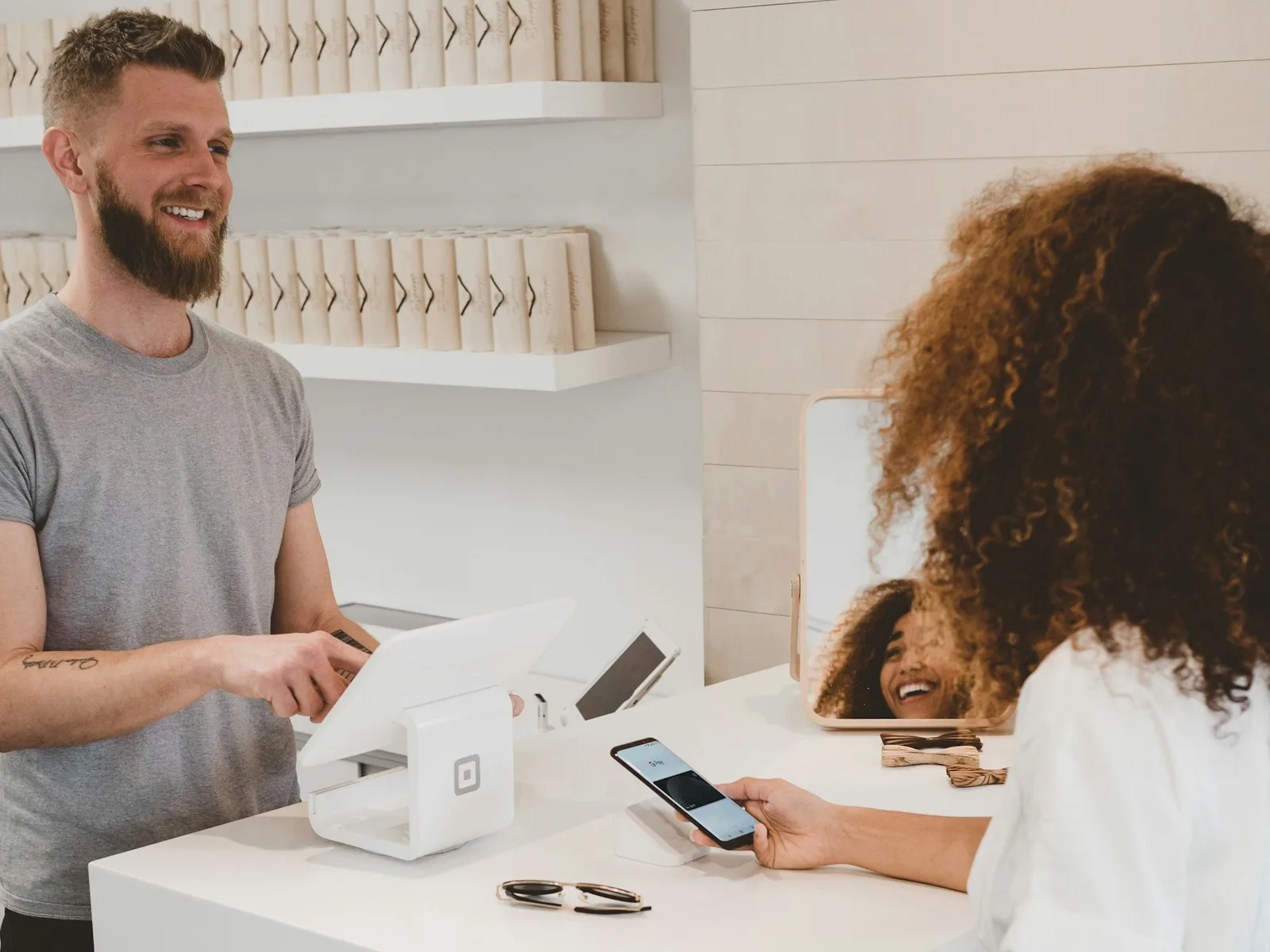 A shop owner rings up a customer paying by phone at the counter