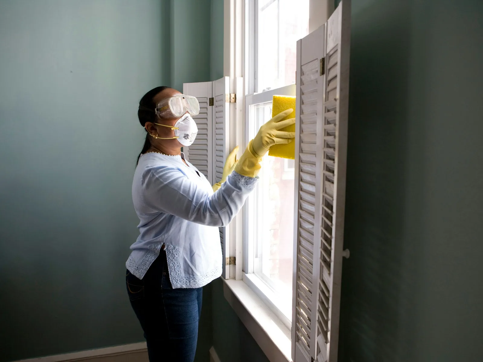 A house cleaner in gloves wipes down window shutters